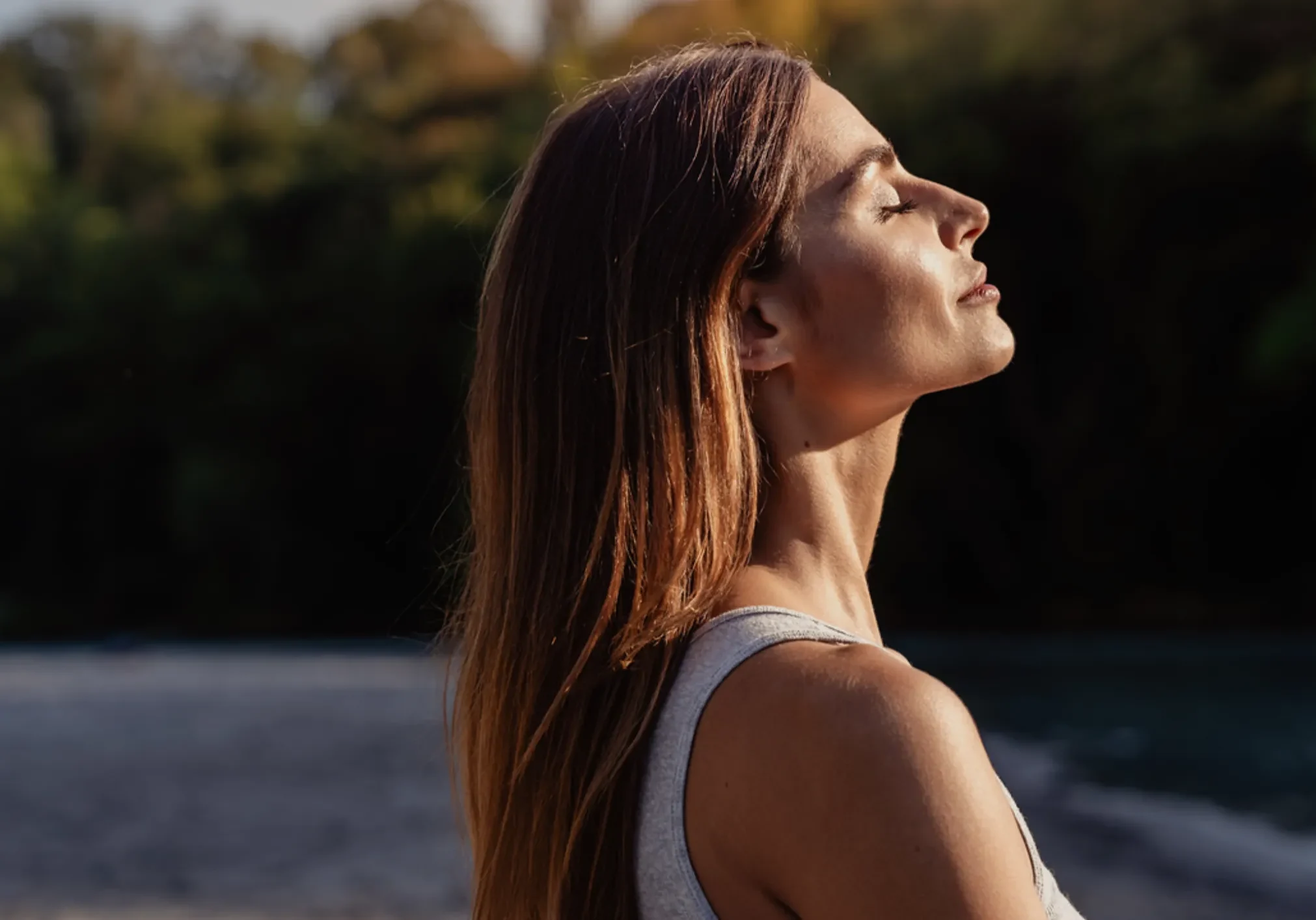 Woman relaxing by river, face turned skyward