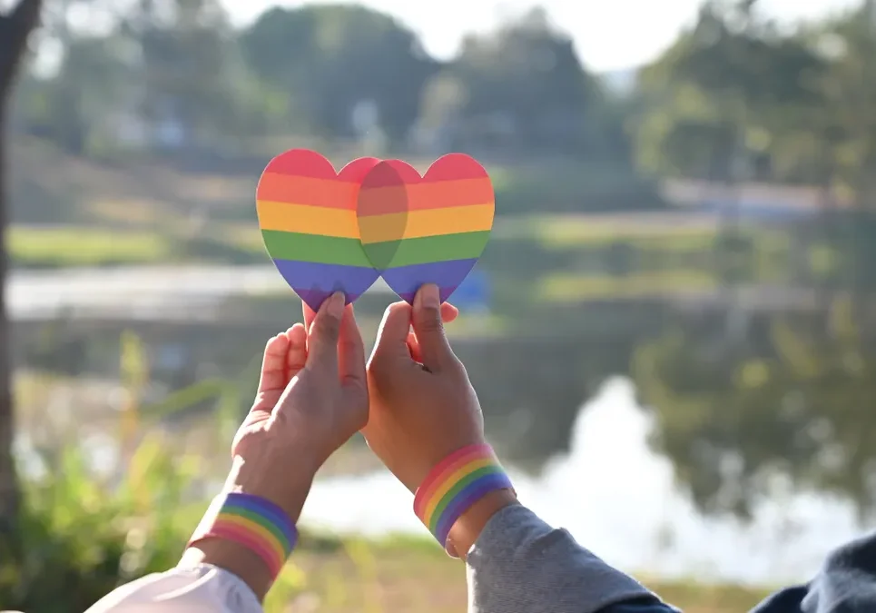 Hands holding rainbow heart cutouts outdoors.